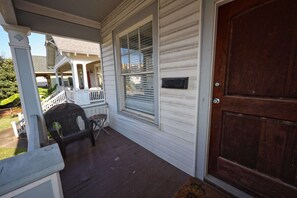 A porch with a wooden door, a mailbox, and a small table with chairs. - Uptown Cottage | Near Strand +Postoffice + UTMB (Galveston)
