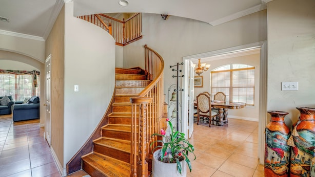 Amplia sala de estar con una escalera de madera, una planta grande en maceta y jarrones decorativos.
