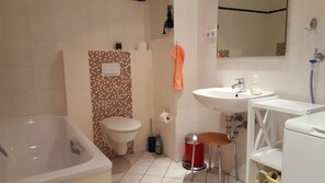 A bathroom with a bathtub, toilet, sink, and a small stool. - Alter Reichshof, App. 302 - with balcony and sea view - Alter Reichshof, App. 302 (Sassnitz auf Rügen)