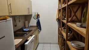 A compact kitchen with a refrigerator, a sink, wooden shelves, and a tiled floor. - Alter Reichshof, App. 302 - with balcony and sea view - Alter Reichshof, App. 302 (Sassnitz auf Rügen)