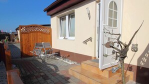 Een huis met houten omheining, een deur en een klein terras met een bankje en een tafel.