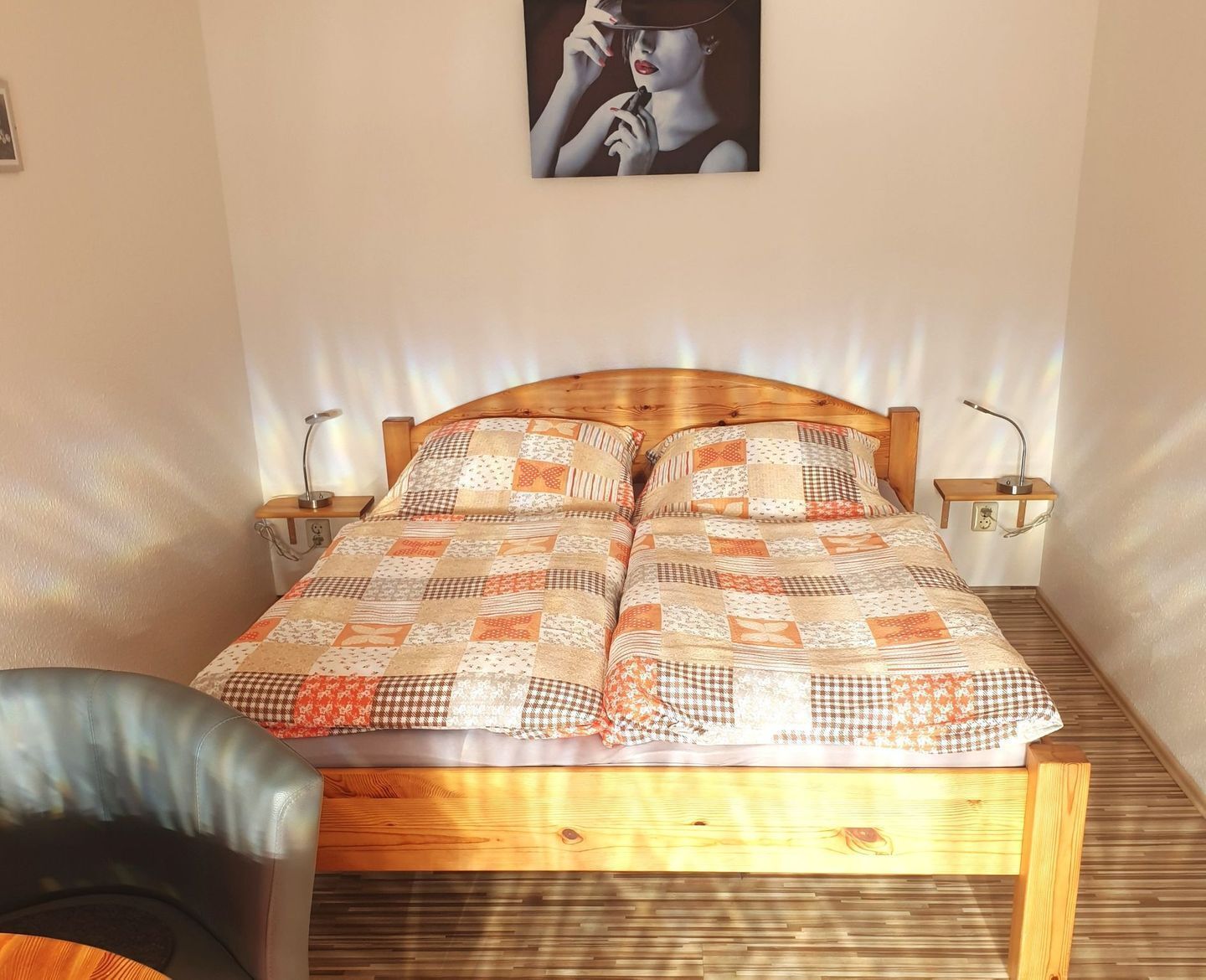 A bed with a wooden headboard, two bedside tables with lamps, a quilt, and a chair.