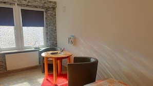 Een kamer met een bed, een klein rond tafeltje met een stoel, een radiator en een raam met jaloezieën.