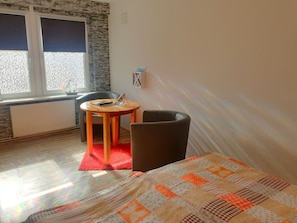 Ein Zimmer mit einem Bett, einem kleinen runden Tisch mit Stuhl, einem Heizkörper und einem Fenster mit Jalousien.