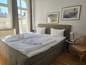 Ein Bett mit weißer Bettwäsche, einem grauen Kopfteil und zwei gerahmten Bildern an der Wand.