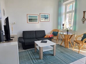 Ein Wohnzimmer mit Sofa, Couchtisch, Fernseher und einem Essbereich mit Stühlen und Tisch.