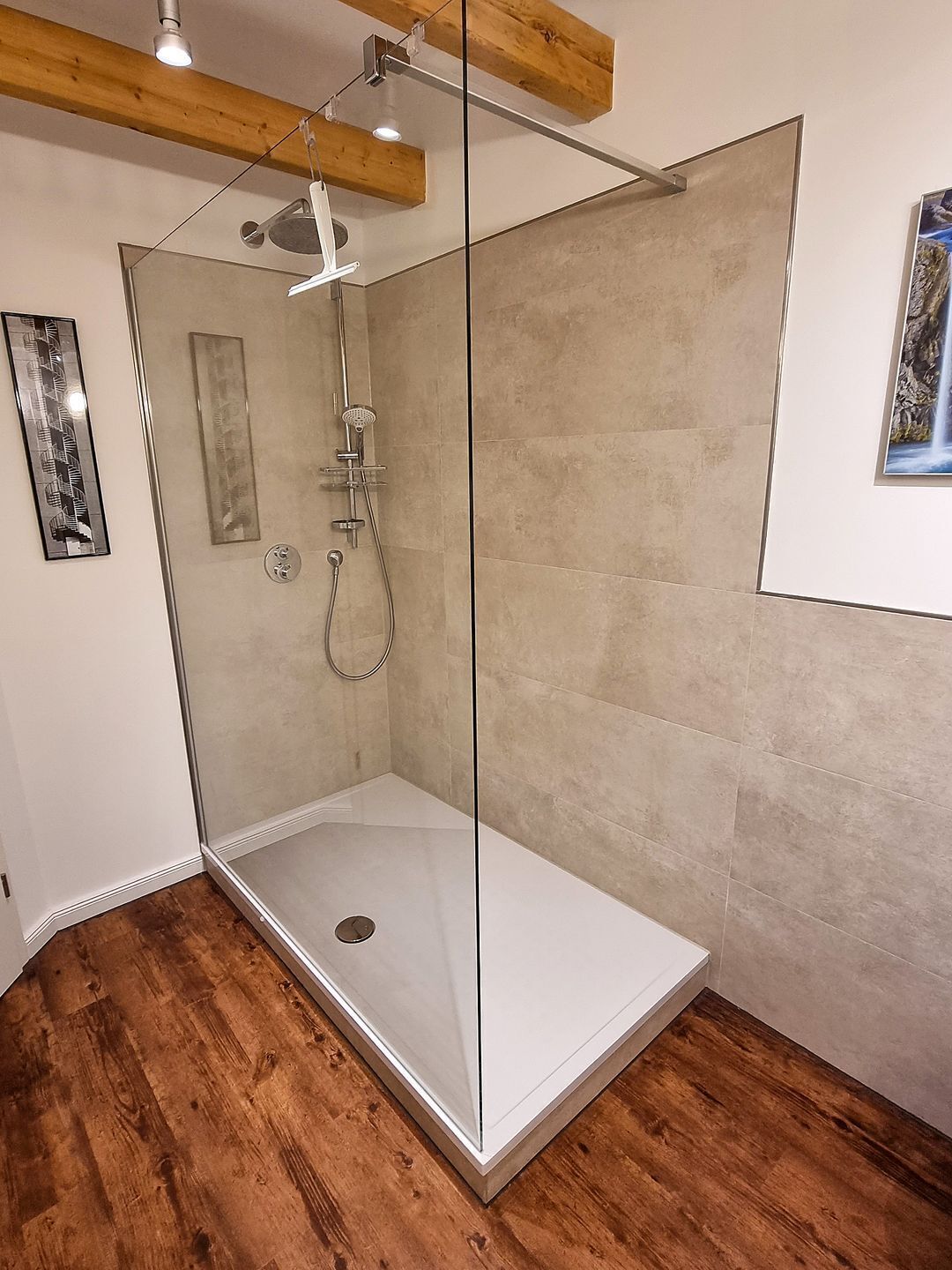 A modern shower enclosure with a glass door, wooden beams, and a tiled floor.