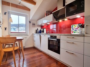 Eine moderne Küche mit weißen Schränken, einer roten Spritzschutzwand und einem Fenster mit Blick.