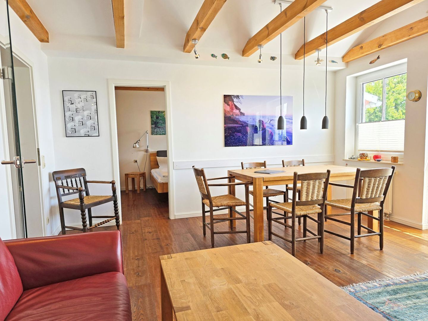 A spacious room with a wooden dining table, chairs, a red sofa, and a large painting on the wall.