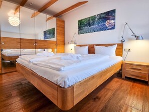 Ein modernes Schlafzimmer mit einem großen Bett, einem Holzkopfstück, Nachttischen mit Lampen und einem großen Spiegel.