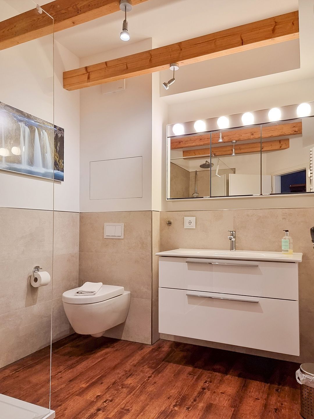 Une salle de bain moderne avec un plafond en bois, un grand miroir avec éclairage intégré, des toilettes et un lavabo avec un meuble-vasque.