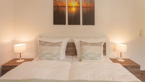 Ein Doppelbett mit zwei Nachttischen, jeder mit einer Lampe, und einem Bild darüber.