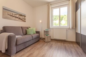 Ein Wohnzimmer mit einer Couch, einer Stehlampe, einem Fenster mit Vorhängen, einer Heizung und einem Bild an der Wand.