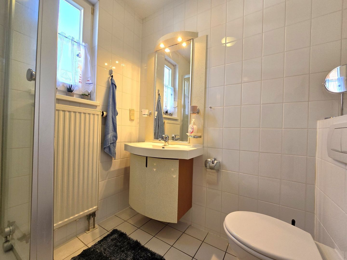 Kylpyhuone, jossa on valkoinen pesuallas, peili, wc-istuin ja ikkuna.