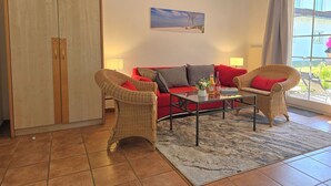 A living room with a red sofa, wicker chairs, a coffee table, and a painting on the wall.