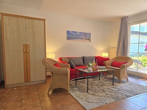 Ein Wohnzimmer mit einem roten Sofa, Korbstühlen, einem Couchtisch und einem Gemälde an der Wand.