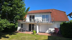 A two-story house with a red-tiled roof, a balcony, and a patio area with outdoor furniture.