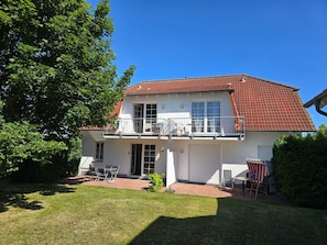 Ein zweistöckiges Haus mit rotem Ziegeldach, einem Balkon und einer Terrasse mit Gartenmöbeln.