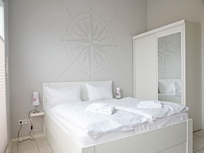 Ein weißes Bett mit Kissen, einer Nachttischlampe und einem Wandbild mit Kompassdesign.