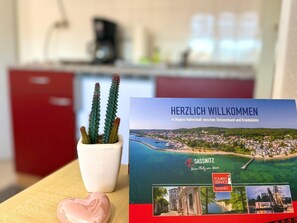 Eine Willkommenskarte für Sassnitz mit Blick auf die Küstenstadt, einem Topf mit Kaktus und einem herzförmigen Gegenstand.