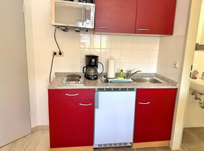 Eine kompakte Küche mit Geschirrspüler, Kaffeemaschine und Mikrowelle.