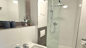 Ein Badezimmer mit einem weißen Waschbecken, einem Spiegel, einer Dusche und einer Toilette.