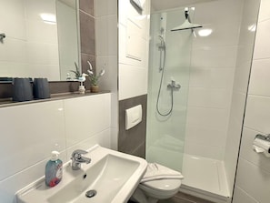Ein Badezimmer mit einem weißen Waschbecken, einem Spiegel, einer Dusche und einer Toilette.