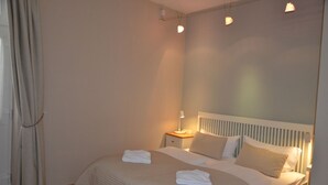 Ein Schlafzimmer mit einem Bett, einem Nachttisch, einer Lampe und einem Fenster mit Vorhängen.