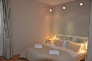 A bedroom with a bed, a nightstand, a lamp, and a window with curtains. - Fürstenhof, App. Sirius 203 - First row by the sea (Sassnitz auf Rügen)