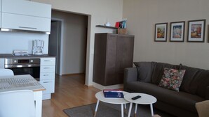Ein modernes Wohnzimmer mit einer Couch, einem kleinen Tisch, einer Küchenzeile mit Kaffeemaschine und einem Schrank.