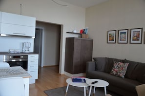 A modern living room with a sofa, a small table, a kitchen area with a coffee machine, and a cabinet. - Fürstenhof, App. Sirius 203 - First row by the sea (Sassnitz auf Rügen)