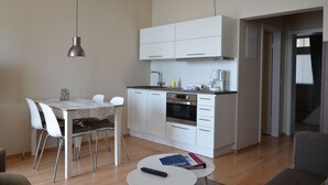 Eine kleine Küche mit weißen Schränken, einem Esstisch mit Stühlen, einer Kaffeemaschine und einer Fernbedienung auf einem kleinen Tisch.