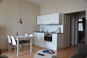 A compact kitchen with white cabinets, a dining table with chairs, a coffee maker, and a remote control on a small table. - Fürstenhof, App. Sirius 203 - First row by the sea (Sassnitz auf Rügen)