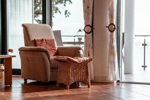 Una habitació amb una finestra gran, una cadira de vimet, una taula petita i una cortina amb dibuixos circulars.