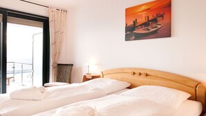 A hotel room with two beds, a view of the sea, a painting of a sunset, and a small table with a lamp. - Villa Friede-Marie, App. Meeresidyll - with wonderful Baltic Sea view and balcony (Sassnitz auf Rügen)