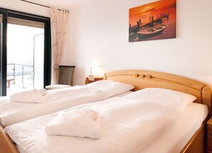 A hotel room with two beds, a view of the sea, a painting of a sunset, and a small table with a lamp. - Villa Friede-Marie, App. Meeresidyll - with wonderful Baltic Sea view and balcony (Sassnitz auf Rügen)