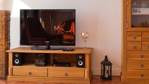 A television on a wooden stand with speakers, a remote control, and a wine glass beside it. - Villa Friede-Marie, App. Meeresidyll - with wonderful Baltic Sea view and balcony (Sassnitz auf Rügen)