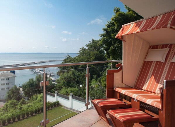 A balcony with a view of a marina and a bridge, a wooden bench with striped cushions, and a clear sky. - Villa Friede-Marie, App. Meeresidyll - with wonderful Baltic Sea view and balcony (Sassnitz auf Rügen)