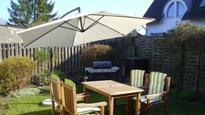 Ein Holzespeiseset im Freien mit großem Sonnenschirm, Grill und einem Holzzaun im Hintergrund.