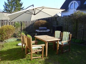 Ein Holzespeiseset im Freien mit großem Sonnenschirm, Grill und einem Holzzaun im Hintergrund.
