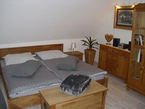 Ein ordentlich eingerichtetes Schlafzimmer mit Bett, Nachttisch, Lampe, Blumentopf, Holzkommode und einem gerahmten Bild an der Wand.
