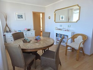 Un coin repas avec une table ronde, des chaises en osier, une bibliothèque et un miroir.