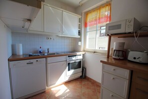 Eine Küche mit weißen Schränken, einem Geschirrspüler, einem Backofen, einer Mikrowelle und einer Kaffeemaschine.