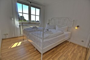 Ein Zimmer mit einem Einzelbett, einem Metall-Kopfteil, weißer Bettwäsche, einem Fenster mit Vorhängen und einem Holzboden.