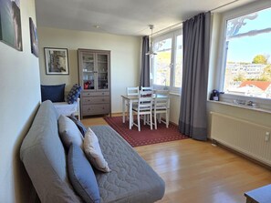 Ein Zimmer mit einem Bett, einem Esstisch mit Stühlen, einem Schrank und einem Fenster mit Vorhängen.