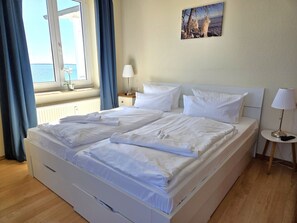 Ein Hotelzimmer mit Bett, Nachttisch, Lampe, einem Fenster mit Vorhängen und einem Bild an der Wand.