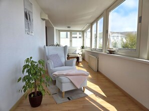 Ein heller Raum mit großem Fenster, einem Sessel, einer Pflanze und einer Heizung.