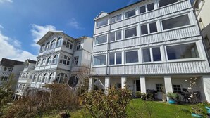 A multi-story building with balconies, a garden area with potted plants, and a clear blue sky. - Villa Johanna, App.2 - Bathing villa with magnificent sea view - Villa Johanna, App. (Sassnitz auf Rügen)