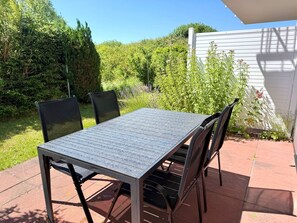 An outdoor patio with a table and chairs, surrounded by greenery and a white building. - Vacation apartment Max - vacation in a quiet location with dog (Neddesitz auf Rügen)