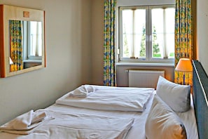 A hotel room with a bed, a mirror, a window with curtains, a radiator, and a lamp. - Vacation apartment Max - vacation in a quiet location with dog (Neddesitz auf Rügen)